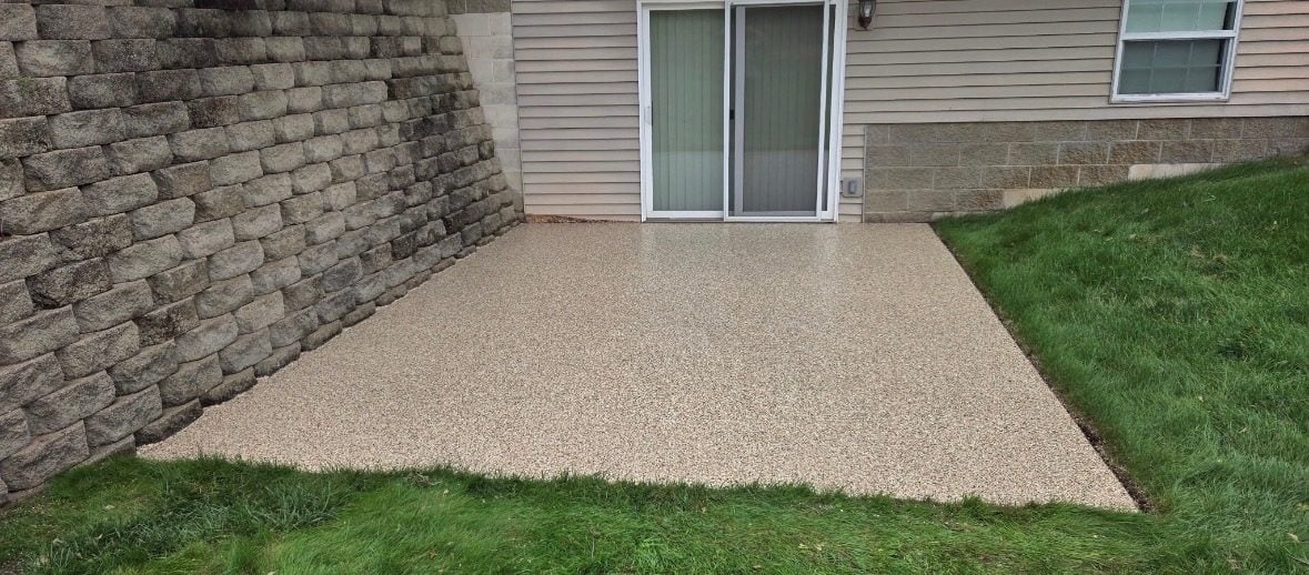 Tan and beige flake coating on a backyard patio slab beside a block retaining wall