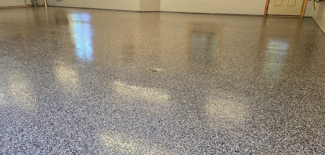 Glossy gray, tan and white flake garage floor reflecting overhead light near a service door