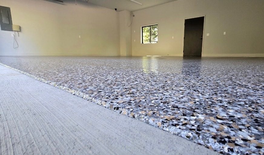Black, tan and white flake garage floor meeting the bare concrete apron at the door