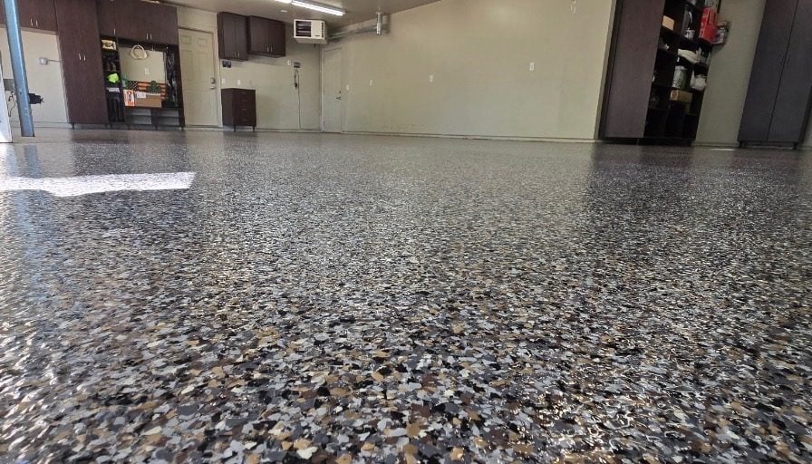 Black, gray and tan flake garage floor beside dark storage cabinets and a workbench
