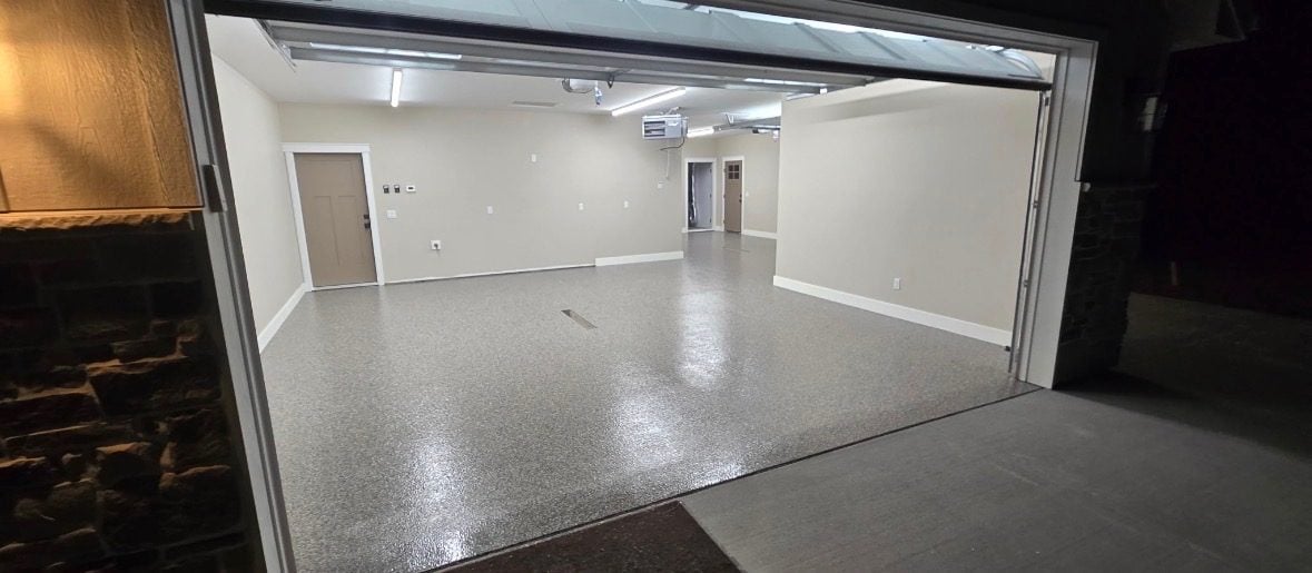 Gray and white flake garage floor seen through open overhead doors at dusk