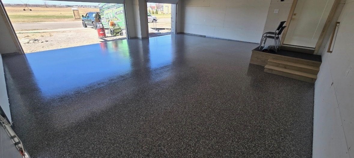 Brown and tan flake garage floor with the door open to farmland and a work truck