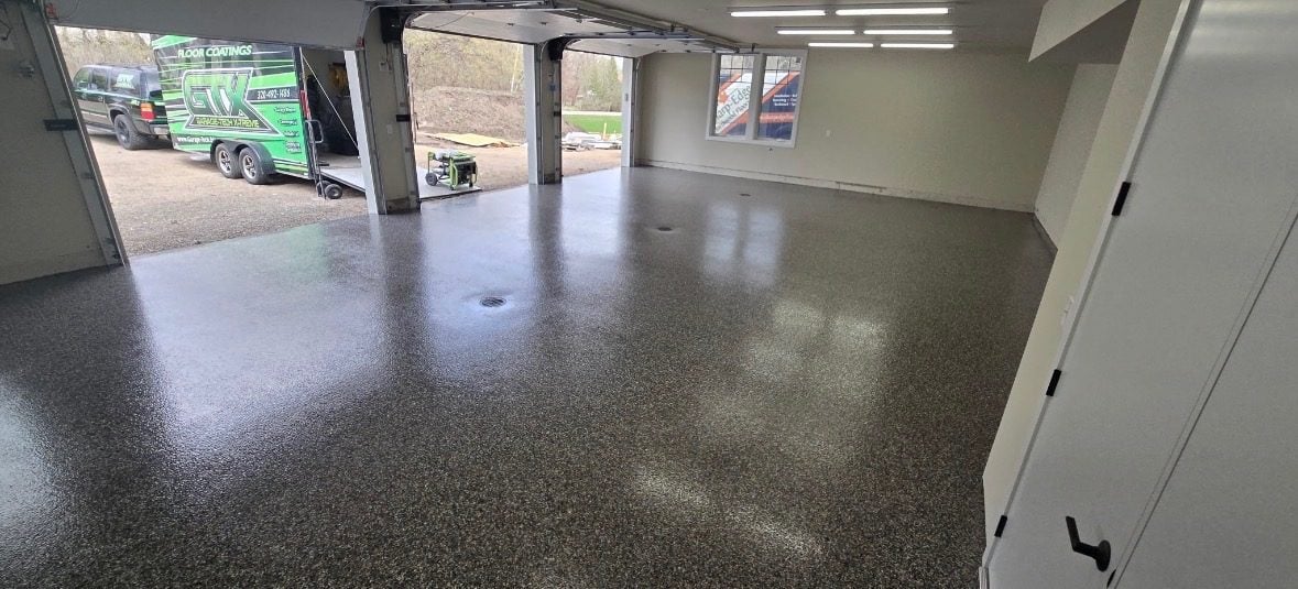 Tan and brown flake floor in a three-stall garage with the doors open to the driveway