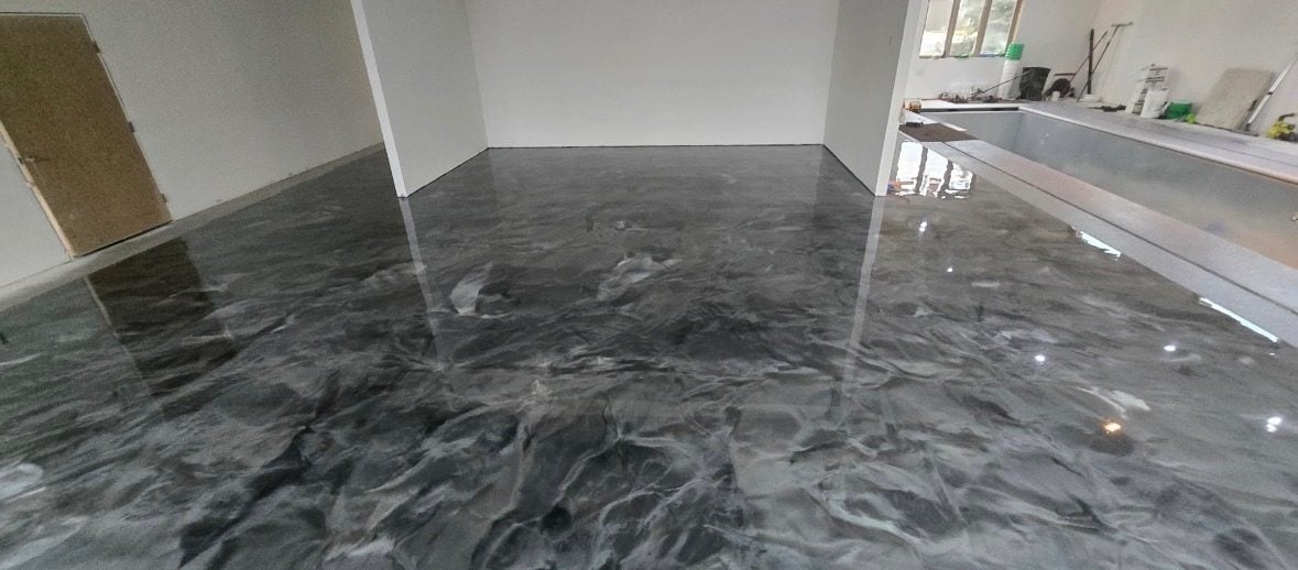 Glossy silver-gray metallic epoxy floor with marbled swirls reflecting an open interior room