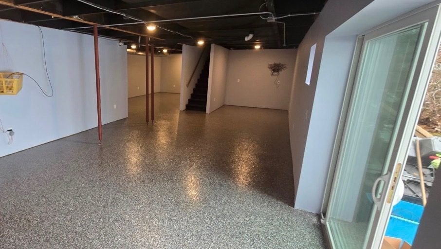 Gray and tan flake coating across a wide finished basement with support posts